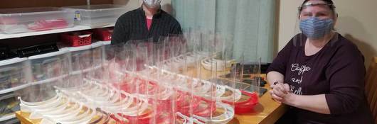 Ed and Brandi Miller sit on either side of a table filled with red and white face shields